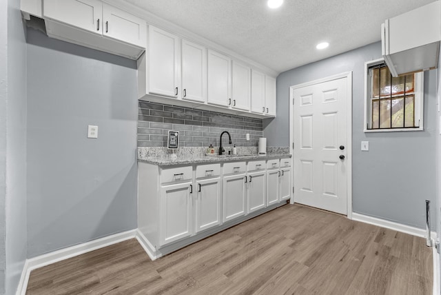 kitchen with light stone counters, white cabinets, sink, backsplash, and light hardwood / wood-style flooring