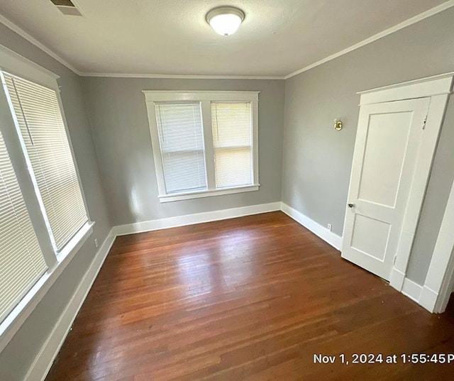 empty room featuring ornamental molding, dark wood-style flooring, and baseboards