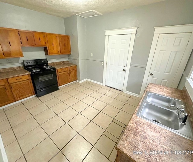 kitchen featuring light tile patterned floors, a textured ceiling, black electric range oven, and sink