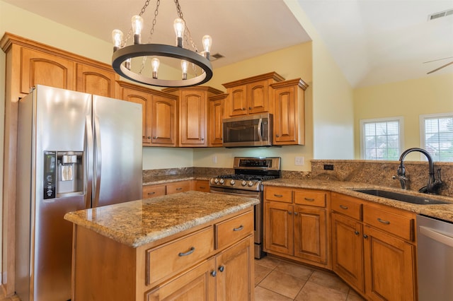 kitchen with sink, appliances with stainless steel finishes, light stone countertops, light tile patterned floors, and a center island