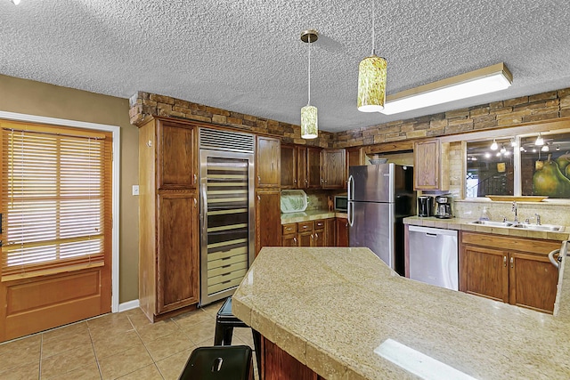 kitchen featuring stainless steel appliances, sink, a textured ceiling, decorative light fixtures, and beverage cooler