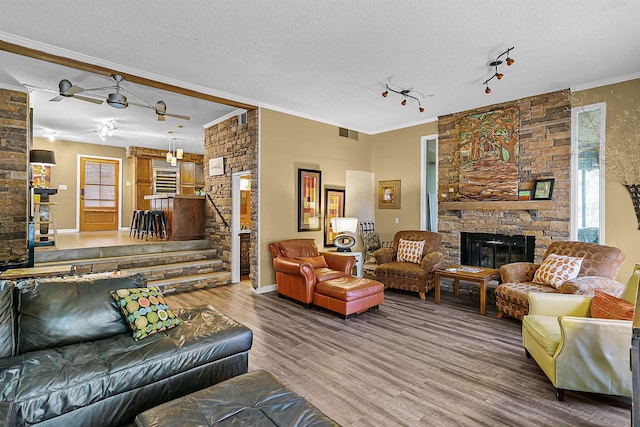 living room with a stone fireplace, wood-type flooring, a textured ceiling, rail lighting, and crown molding