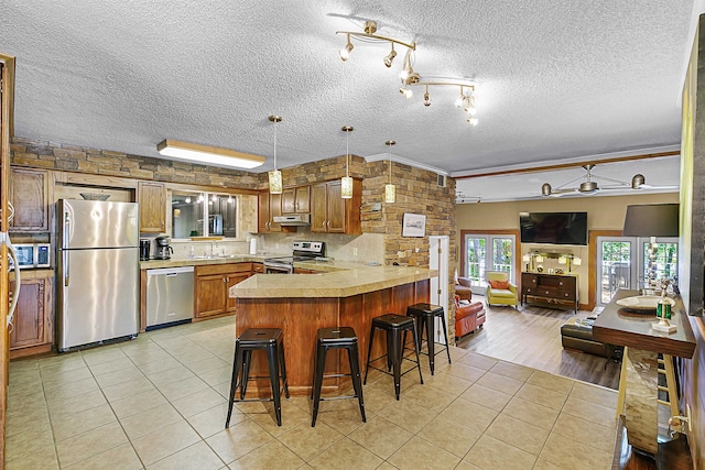 kitchen with stainless steel appliances, light hardwood / wood-style floors, a breakfast bar, kitchen peninsula, and a textured ceiling