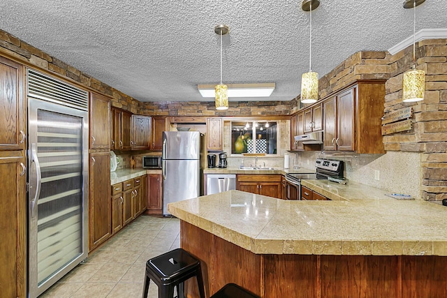 kitchen featuring stainless steel appliances, a textured ceiling, pendant lighting, a breakfast bar, and kitchen peninsula