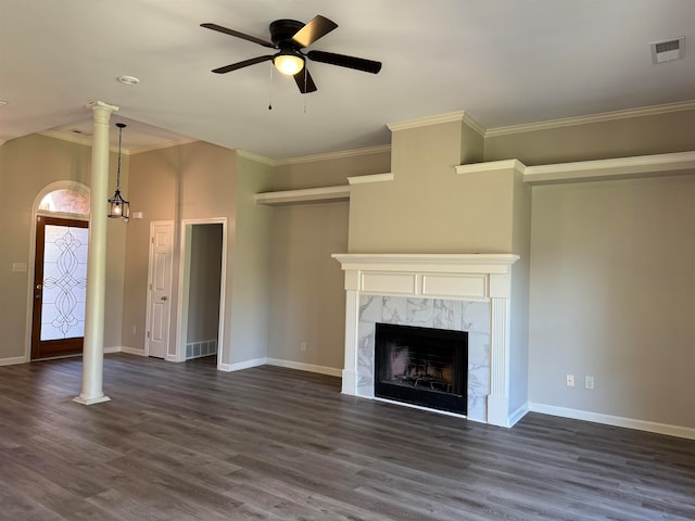 unfurnished living room featuring crown molding, ceiling fan, a premium fireplace, dark hardwood / wood-style flooring, and decorative columns