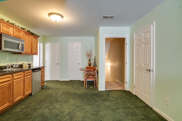 kitchen featuring dark stone countertops, dark colored carpet, sink, and appliances with stainless steel finishes