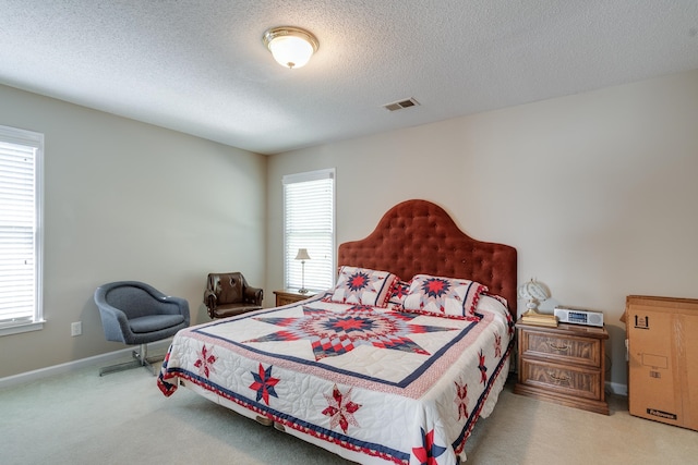 bedroom featuring multiple windows, a textured ceiling, and light carpet