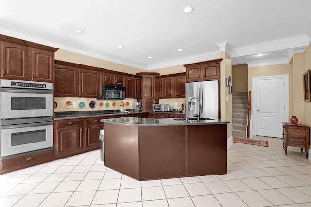 kitchen featuring an island with sink, sink, dark stone counters, dark brown cabinetry, and stainless steel appliances