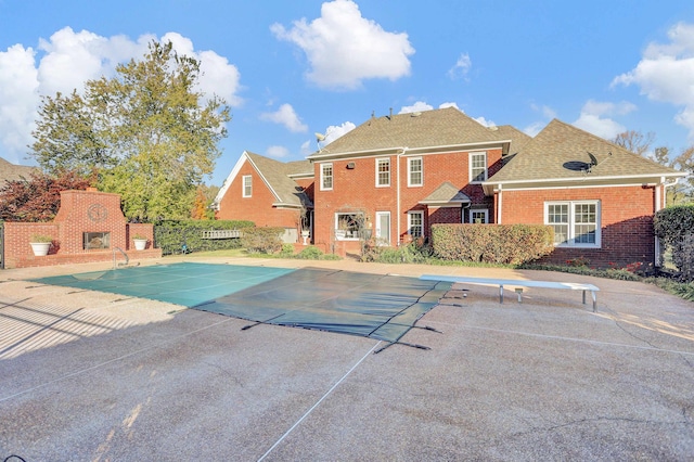 view of pool with an outdoor brick fireplace, a diving board, and a patio area