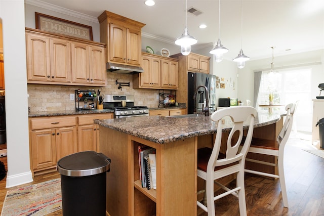 kitchen featuring appliances with stainless steel finishes, a breakfast bar area, decorative light fixtures, an island with sink, and hardwood / wood-style floors