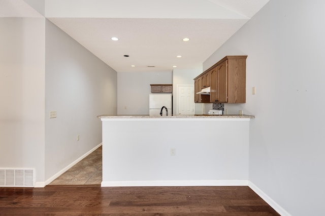 kitchen with dark wood-type flooring, white refrigerator, and kitchen peninsula