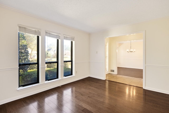 empty room featuring dark wood-type flooring, an inviting chandelier, crown molding, and a textured ceiling