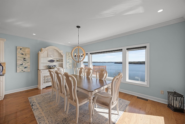 dining area with light hardwood / wood-style floors, a water view, crown molding, and a notable chandelier