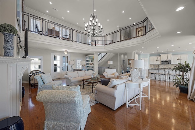 living room with dark wood-type flooring, a towering ceiling, a chandelier, and crown molding