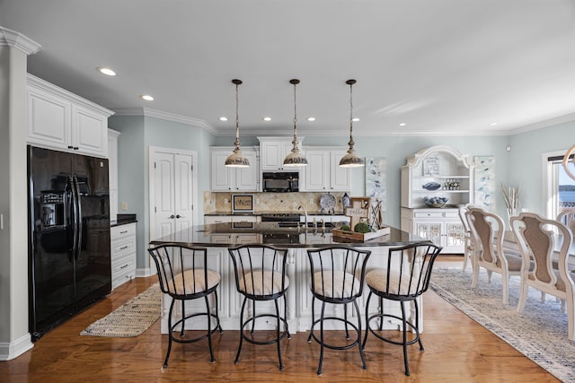 kitchen with white cabinets, hardwood / wood-style flooring, a center island with sink, and black appliances