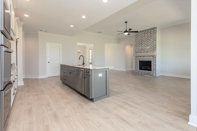 kitchen featuring sink, a fireplace, an island with sink, light hardwood / wood-style floors, and stainless steel appliances