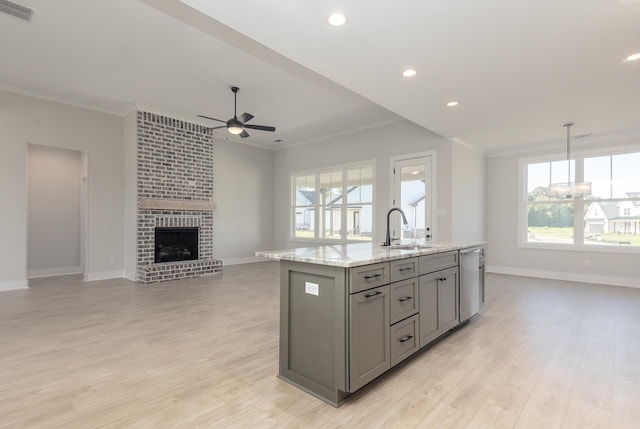 kitchen featuring sink, a brick fireplace, an island with sink, light hardwood / wood-style floors, and gray cabinets