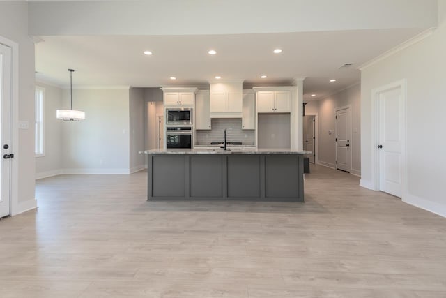 kitchen featuring light stone countertops, appliances with stainless steel finishes, an island with sink, white cabinets, and ornamental molding