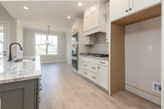 kitchen featuring sink, stainless steel appliances, light stone counters, decorative light fixtures, and white cabinets