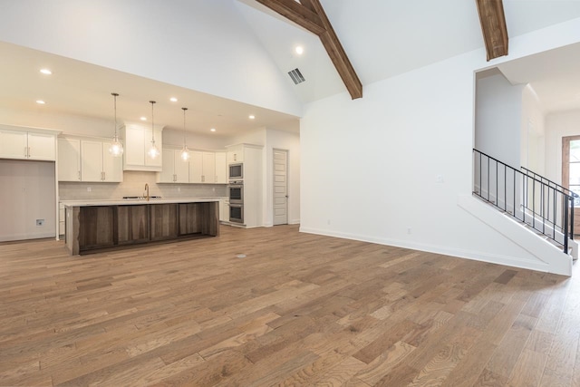 unfurnished living room with beamed ceiling, sink, high vaulted ceiling, and light wood-type flooring