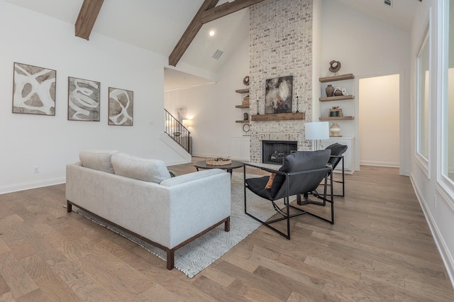 living room with beam ceiling, a brick fireplace, high vaulted ceiling, and light hardwood / wood-style flooring