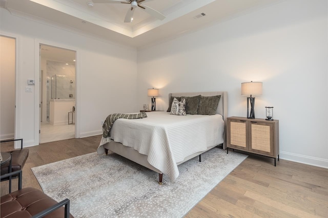 bedroom featuring connected bathroom, a tray ceiling, light hardwood / wood-style flooring, and ceiling fan