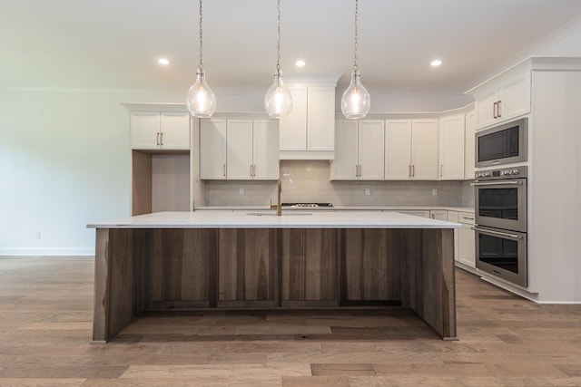 kitchen featuring a center island with sink, white cabinetry, hanging light fixtures, and light hardwood / wood-style floors