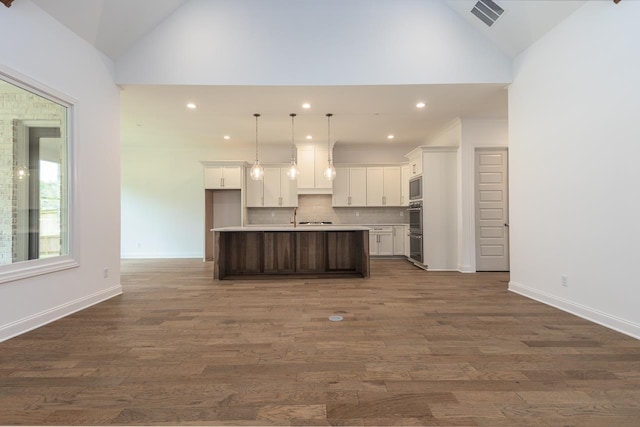 kitchen with white cabinets, decorative light fixtures, a center island with sink, and dark wood-type flooring