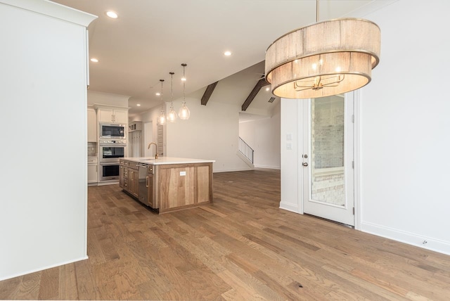 kitchen featuring sink, stainless steel appliances, an island with sink, decorative light fixtures, and light wood-type flooring