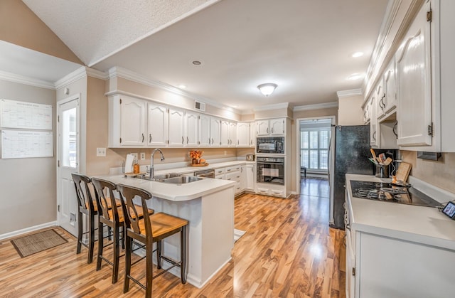 kitchen featuring white cabinetry, sink, ornamental molding, black appliances, and light wood-type flooring