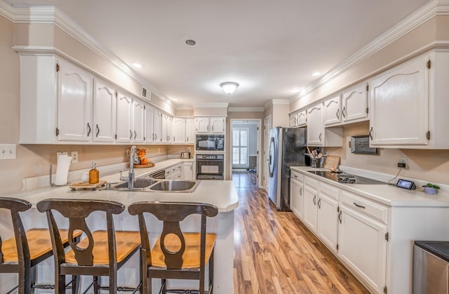 kitchen with light hardwood / wood-style flooring, kitchen peninsula, a breakfast bar, white cabinets, and black appliances