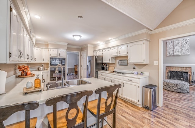 kitchen with sink, white cabinets, a brick fireplace, black appliances, and light hardwood / wood-style floors