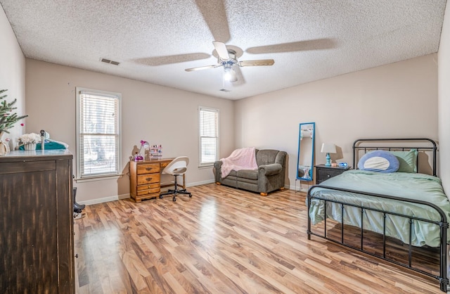 bedroom with multiple windows, a textured ceiling, light hardwood / wood-style floors, and ceiling fan