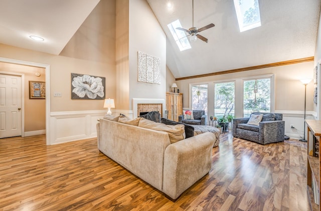 living room featuring a fireplace, hardwood / wood-style floors, high vaulted ceiling, a skylight, and ceiling fan