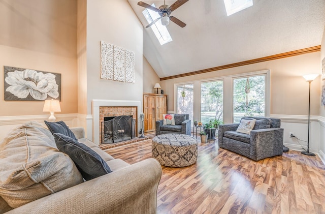 living room with ceiling fan, a brick fireplace, high vaulted ceiling, crown molding, and wood-type flooring