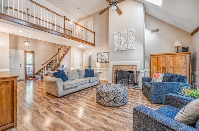 living room with hardwood / wood-style floors, high vaulted ceiling, ceiling fan, and a brick fireplace