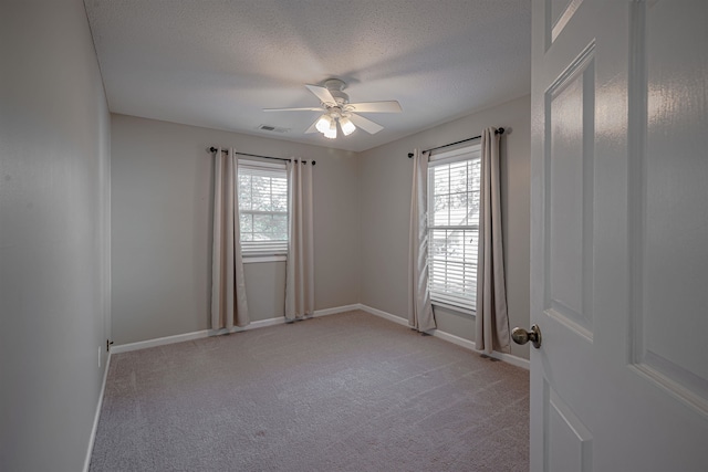 carpeted spare room featuring a textured ceiling, ceiling fan, and a healthy amount of sunlight