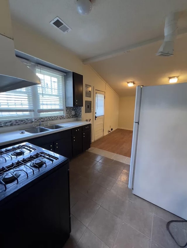 kitchen with white fridge, decorative backsplash, black gas range oven, sink, and lofted ceiling