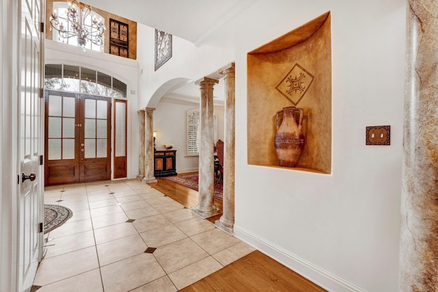 foyer with ornate columns, french doors, ornamental molding, and light wood-type flooring