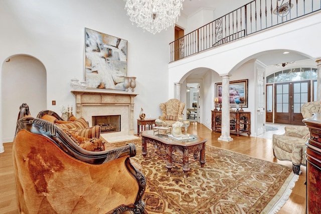 living room with a high end fireplace, decorative columns, a towering ceiling, and light hardwood / wood-style flooring