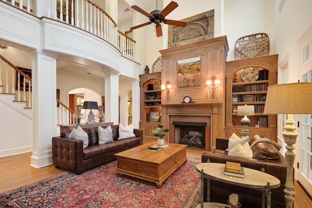 living room featuring decorative columns, built in features, a towering ceiling, and hardwood / wood-style flooring