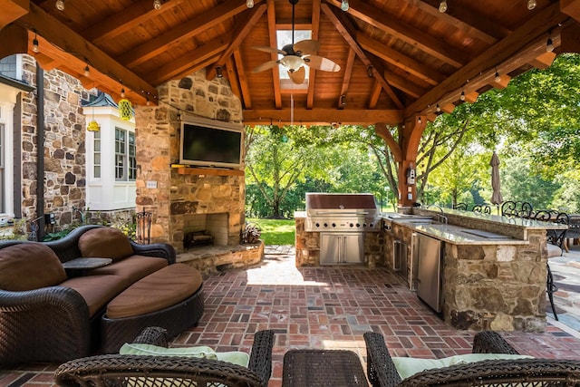 view of patio / terrace with an outdoor kitchen, ceiling fan, an outdoor living space with a fireplace, a gazebo, and a grill