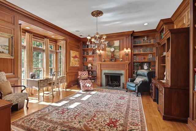 living area with crown molding, wooden walls, built in features, light wood-type flooring, and a notable chandelier