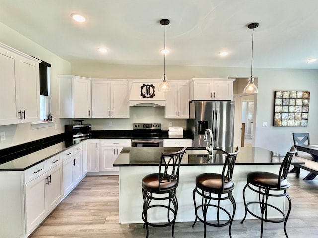 kitchen featuring a kitchen island with sink, white cabinets, hanging light fixtures, light hardwood / wood-style floors, and stainless steel appliances