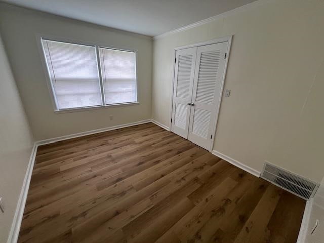 unfurnished bedroom featuring wood-type flooring, a closet, and ornamental molding