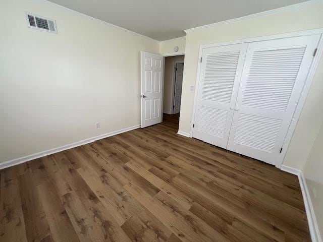 unfurnished bedroom featuring crown molding, dark wood-type flooring, and a closet