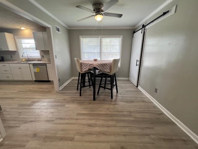 dining room featuring a barn door, ceiling fan, sink, and light wood-type flooring