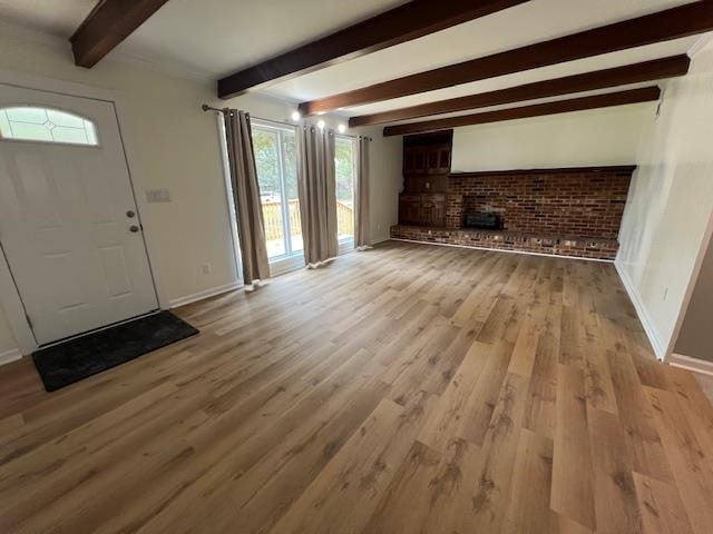 unfurnished living room featuring beamed ceiling, a healthy amount of sunlight, and light hardwood / wood-style flooring