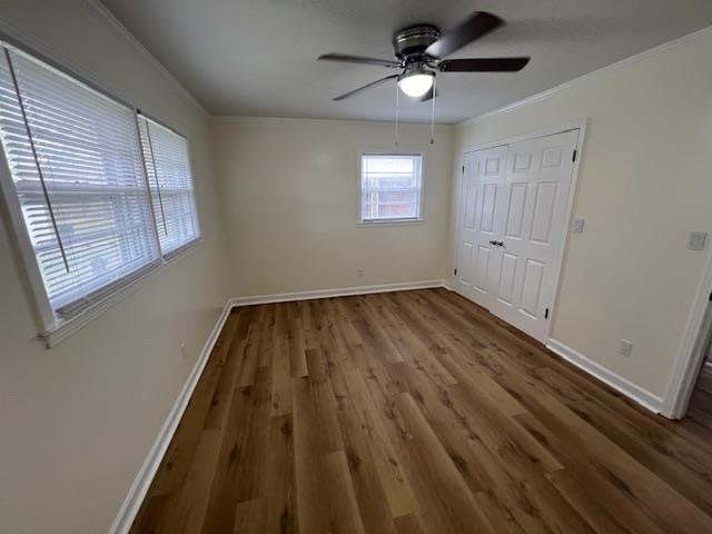 unfurnished bedroom with dark hardwood / wood-style floors, ceiling fan, crown molding, and a closet