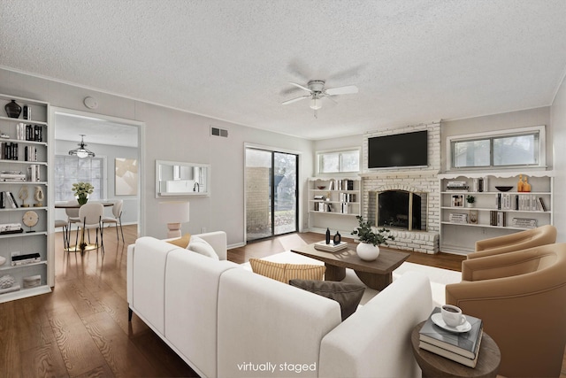 living room with wood finished floors, visible vents, a ceiling fan, a fireplace, and a textured ceiling
